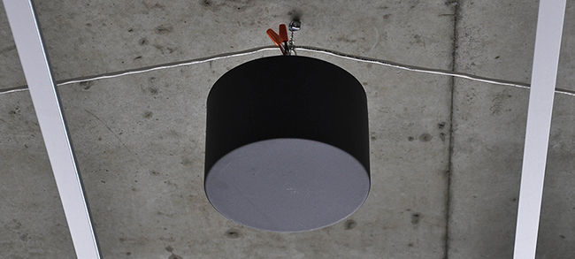 Black sound masking speaker hanging from exposed concrete ceiling
